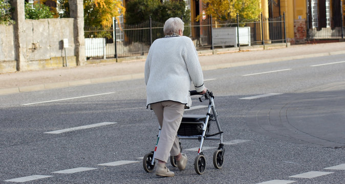 Alte Frau mit Rollator &uuml;berquert die Stra&szlig;e