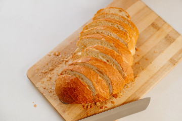 A fresh loaf cut into pieces lies on a wooden board, next to a knife-file for bread. The crust crumbled into crumbs. A fresh French baguette is sliced on a wooden board.