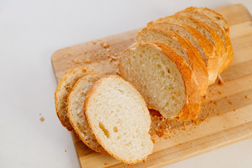 A fresh loaf cut into pieces lies on a wooden board, next to a knife-file for bread. The crust crumbled into crumbs. A fresh French baguette is sliced on a wooden board.