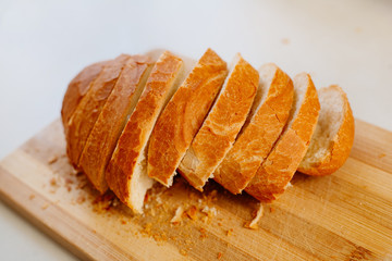 A fresh loaf cut into pieces lies on a wooden board, next to a knife-file for bread. The crust crumbled into crumbs. A fresh French baguette is sliced on a wooden board.