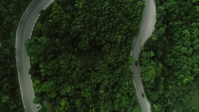 Static top view aerial shot traffic on winding asphalt roads surrounded by hilly terrain and green dense forest cars and motorcycles moving along two two-lane roads view from above