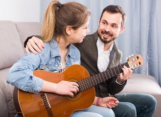 Male tutor assisting teenage pupil in learning how to play guitar