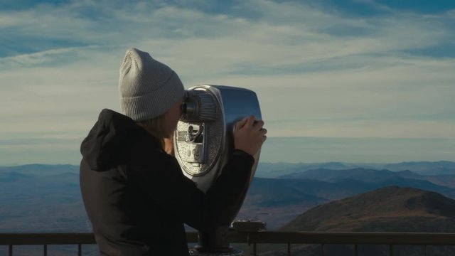 Caucasian female enjoys the view of a mountain valley through coin-operated binoculars at the viewing platform. 4K UHD