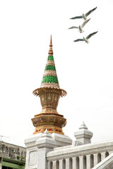Architectural detail from exterior view of the Buddhist temple, Wat Traimit over clear sky with flying seagulls in Bangkok, Thailand