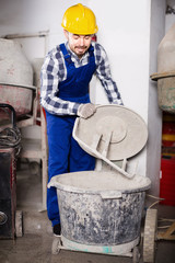 Young positive male using concrete mixer at workplace