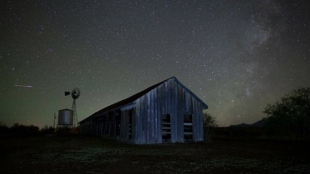 Night time lapse of stars above on old rustic barn