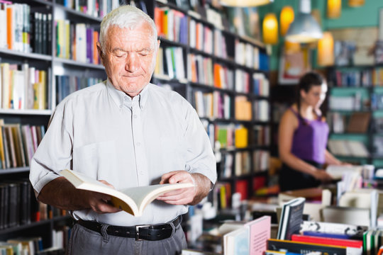 Old male customer is choosing book for reading