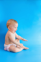 Happy baby on blue background. Girl in white panties sitting and smiling. Copy space. Baby emotions.