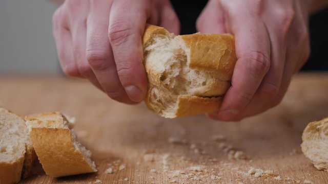 Baker tearing fresh bread on a half. Male hands breaks baguette for inspecting a bread quality at commercial kitchen of bakery, cut cutting knife Close-up.