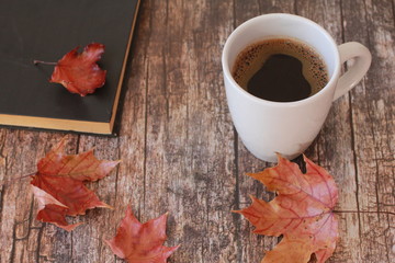 Coffee, book and red maple leaves on vintage wooden background. Autumn drink concept. October, November, fall foliage