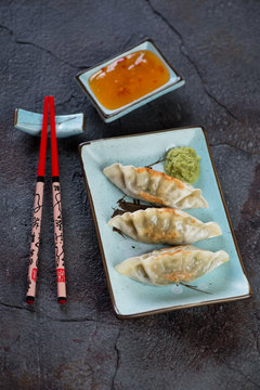 Turquoise tableware with fried korean dumplings and dipping sauce over cracked asphalt background, studio shot
