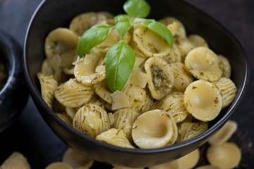 Close-up of italian orecchiette pasta served with basil pesto sauce in a black bowl, selective focus