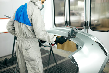 automobile repairman painter in protective clothes with airbrush pulverizer painting car bumper