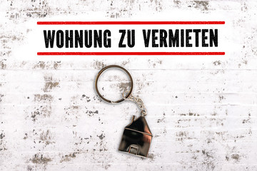 Nachricht "Wohnung zu vermieten" und Schlüsselanhänger in Hausform auf Steinuntergrund