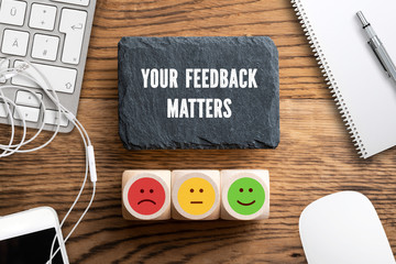 cubes with a emoticons and slate plate with message "your feedback matters" on wooden background