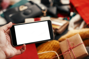 Christmas shopping and sale. Hand holding phone with empty screen on background of credit cards,money, wallet, bags, clothes, gifts, jewelry. Space for text. Advertising app. Black Friday.