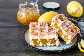 Sweet dessert. Homemade waffles with filling, fresh lemons and a small glass jar with fruit jam on...