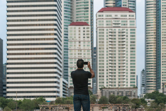 Man Holding A Smart Phone And Taking A Picture With Buildings In The City In Background