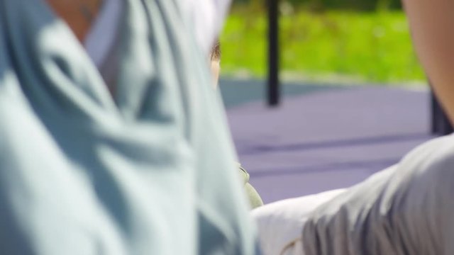 Cheerful little boy holding legs of father and counting reps while dad doing sit ups on bench on outdoor workout playground on sunny day