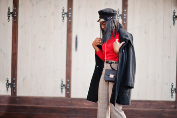 African american fashion girl in coat and newsboy cap posed at street.