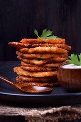 Vegetable pancakes and sour cream topped with parsley leaves on a dark plate