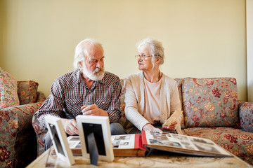 Senior european couple of pensioners sitting in cozy living room looking at photos from their...