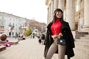 African american fashion girl in coat and newsboy cap posed at street.