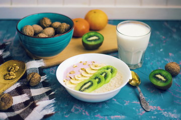 Bowl of oatmeal porridge with nuts banana kiwi and glass of milk on vintage table. Healthy food. Dieat. Morning breakfast.