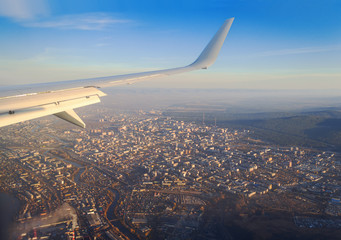 Fototapeta premium view from the airplane window on the river and the city among the mountains at dawn in the rays of the sun