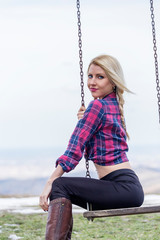 Beautiful blonde girl sitting on swing with nature and snow on background