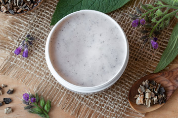 A jar of homemade comfrey root ointment with blooming comfrey plant