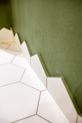 Close-up of the floor corner made with hexagonal white tiles and green walll