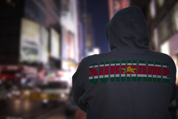 dangerous man standing on a city street with black hoodie with text suriname on his back