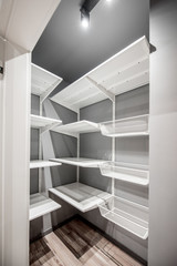 Empty wardrobe room with white metal shelves in the apartment