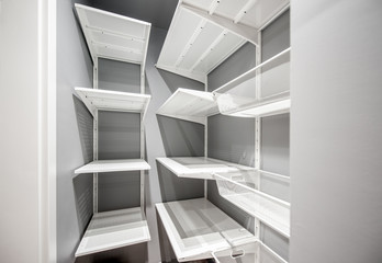 Empty wardrobe room with white metal shelves in the apartment
