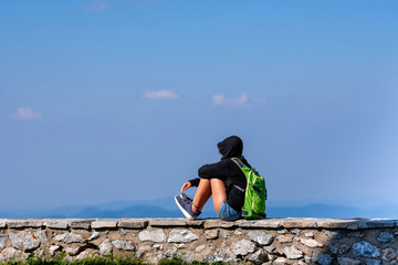 A man with a green backpack sits on a stone wall and relaxes.