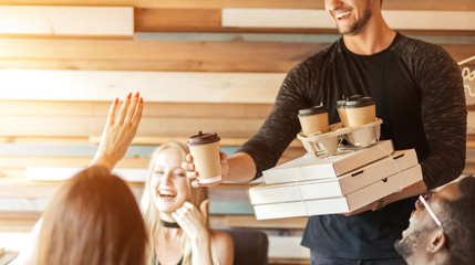 Caucasian sportive man with athletic body handing out food orders to his multiethnic friends at...