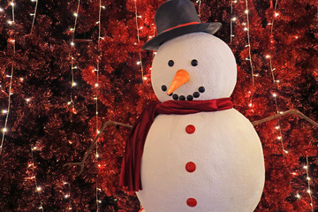 Large snowman in front of sparkling artificial red pine trees for Christmas indoor decoration 