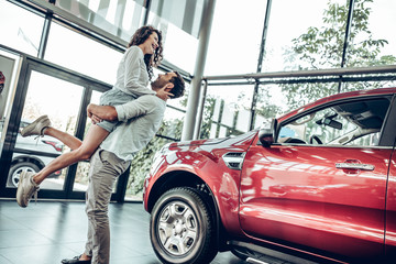 Naklejka na ściany i meble Beautiful young couple is smiling while buying a car in a motor show