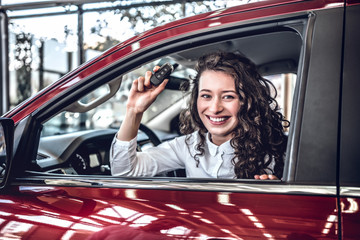 Happy young woman driver holding auto keys in her new modern luxury car