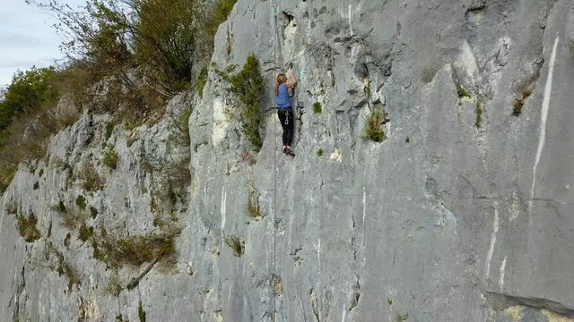 Jeune fille grimpant au sommet d'une falaise film&eacute;e par un drone d'abord en gros plan puis avec un long zoom arri&egrave;re o&ugrave; l'on peut voir toute la falaise.