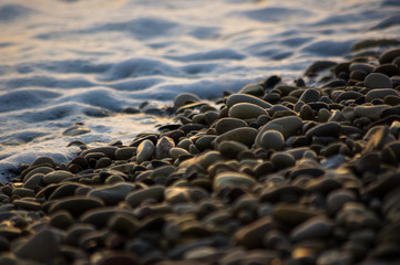 pebble stones on the sea beach, the rolling waves of the sea with foam