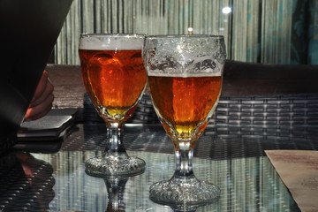 Two glass of glass of beer on the glass table, with one glass just drank.