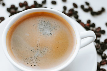 White cup with fresh coffee on saucer close up with grains of coffee on white isolated background