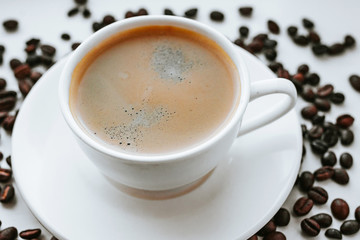 White cup with fresh coffee on saucer close up with grains of coffee on white isolated background