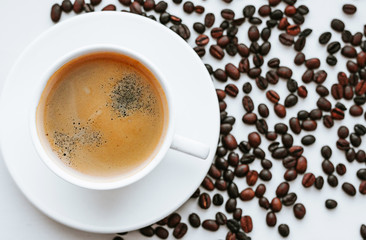 White cup of coffee on saucer close up with beans of coffee on white isolated background, top view