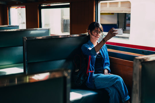 Asian woman traveler sits on train seat and used smart phone selfie photos while wait train leaving station of the railway station - travel and transportation concept