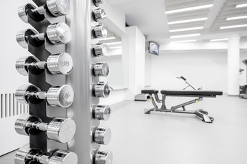 Fototapeta premium Close-up of a stand full of dumbbells at the white gym interior
