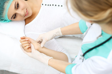 Female doctor and young woman patient in hospital. Physicians examine girl pulse lying at the bed,...