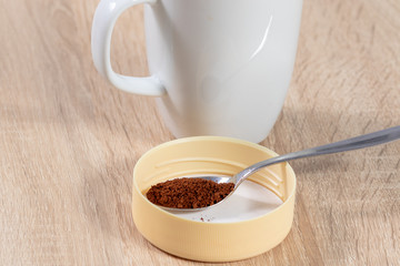 Spoon with instant coffee powder in front of a white cup